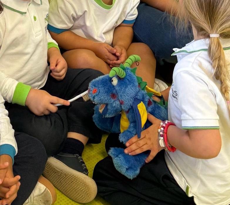 Crianças sentadas em roda com a mascote de dragão e uma escova de dentes